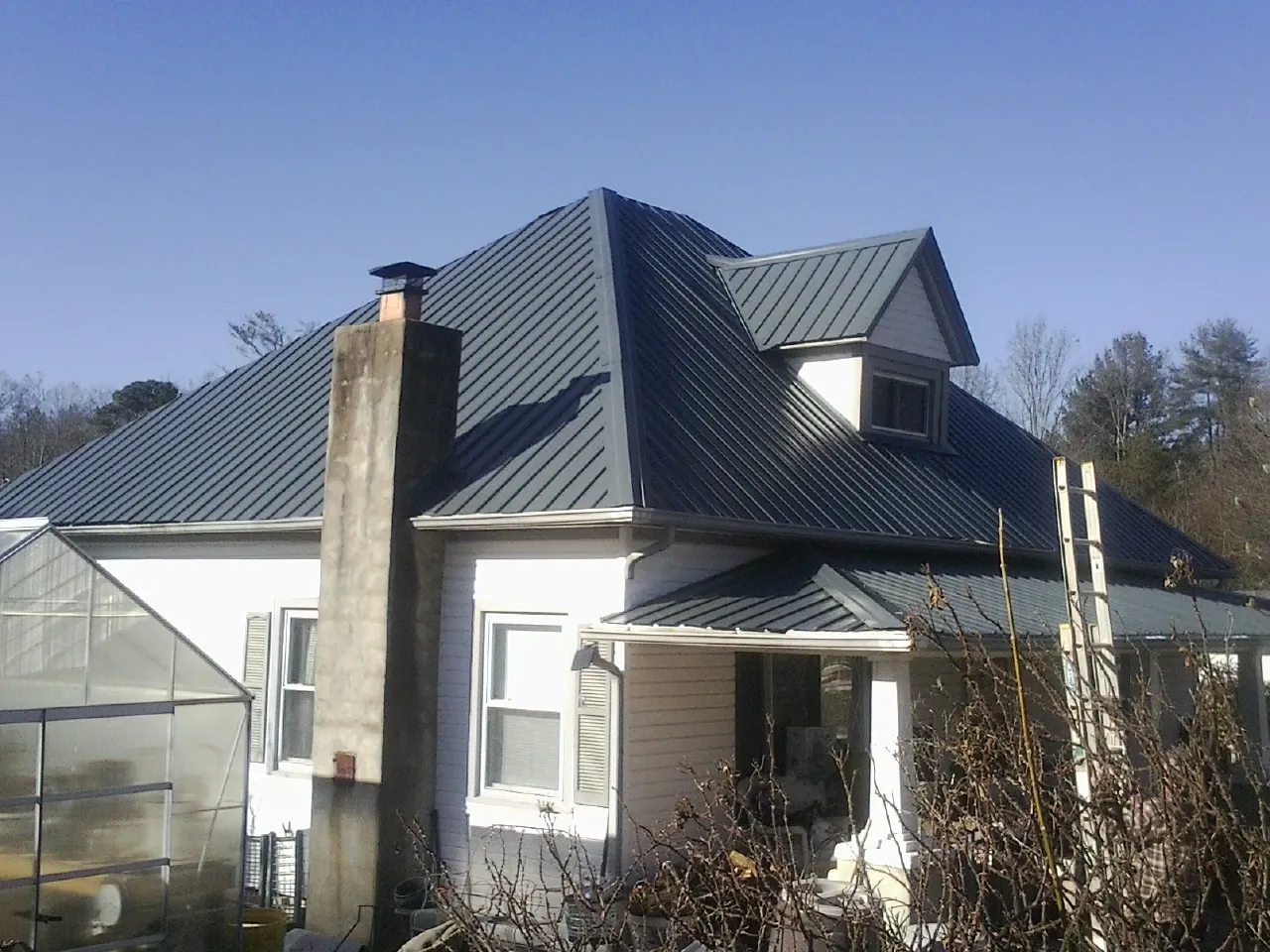 Dark blue standing seam metal roof on a white farmhouse with dormer — Slate & Tile Roof Repair by Roofing Brothers in South Glens Falls