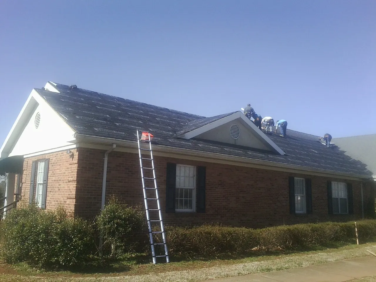Crew tearing shingles off a brick ranch roof with a ladder set — Metal Roof Repair work by our crew in South Glens Falls