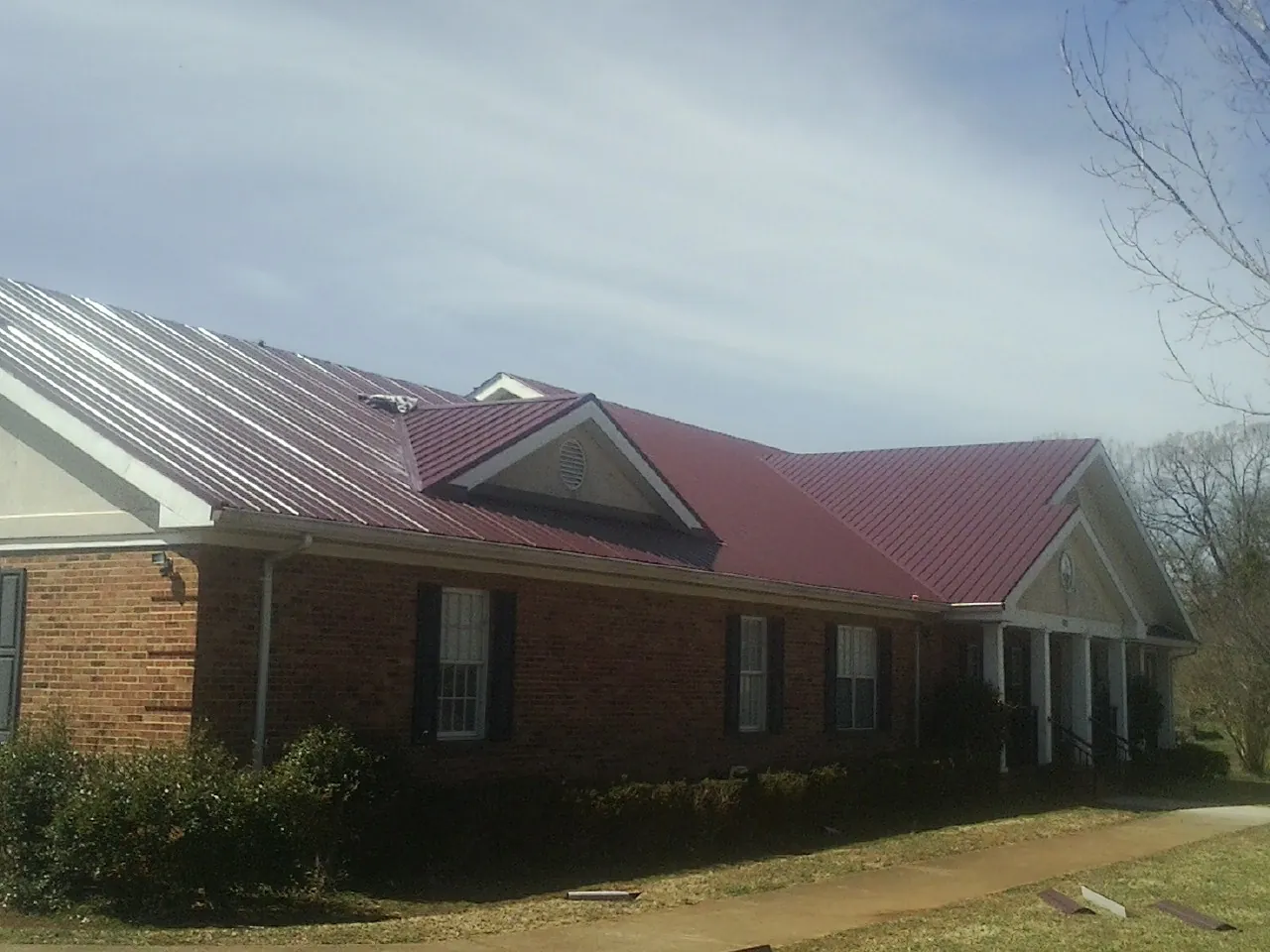 Red metal roof with gabled entries on a long brick building, from a Hail Damage Roof Repair job in South Glens Falls