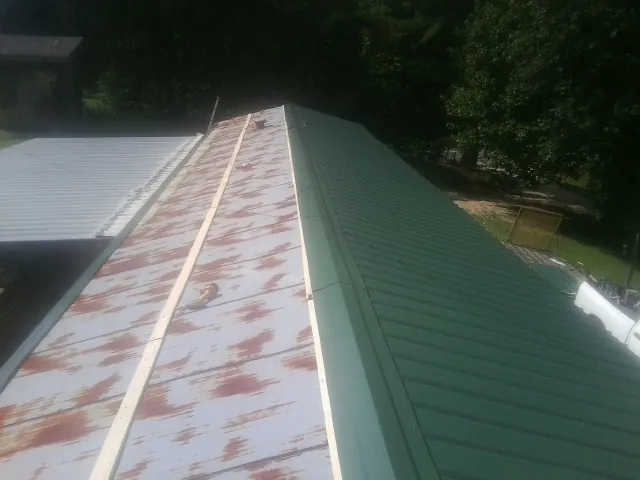 Old rusted panels beside newly installed green metal roofing in South Glens Falls
