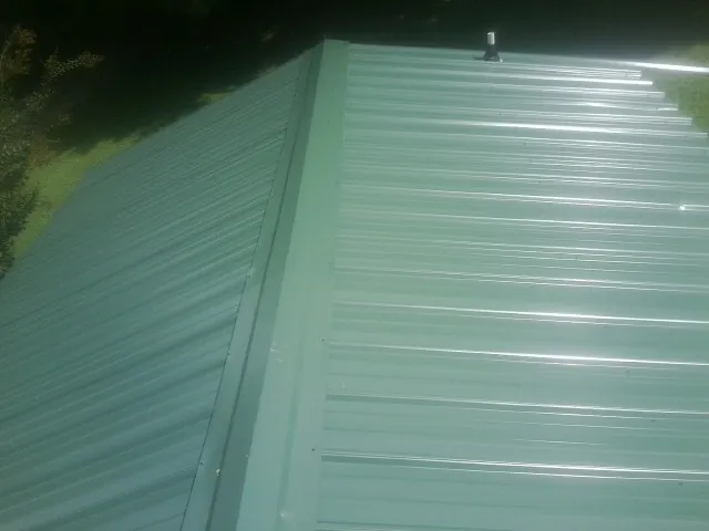 New green metal panels meeting at the ridge of a roof — Flat Roof Repair work by our crew in South Glens Falls