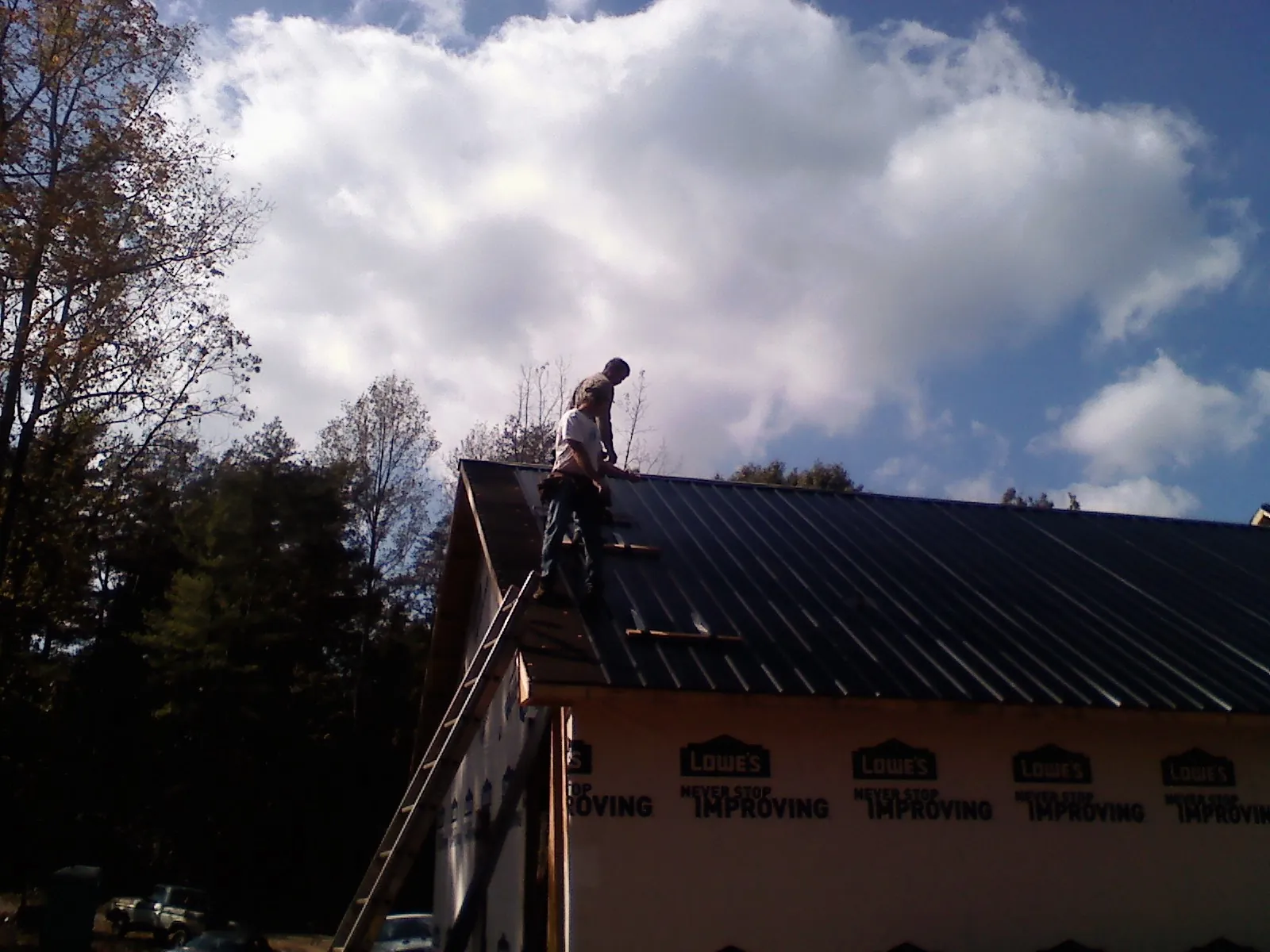 Roofer fastening dark metal panels high against a cloudy sky, from a Roof Inspection job in South Glens Falls