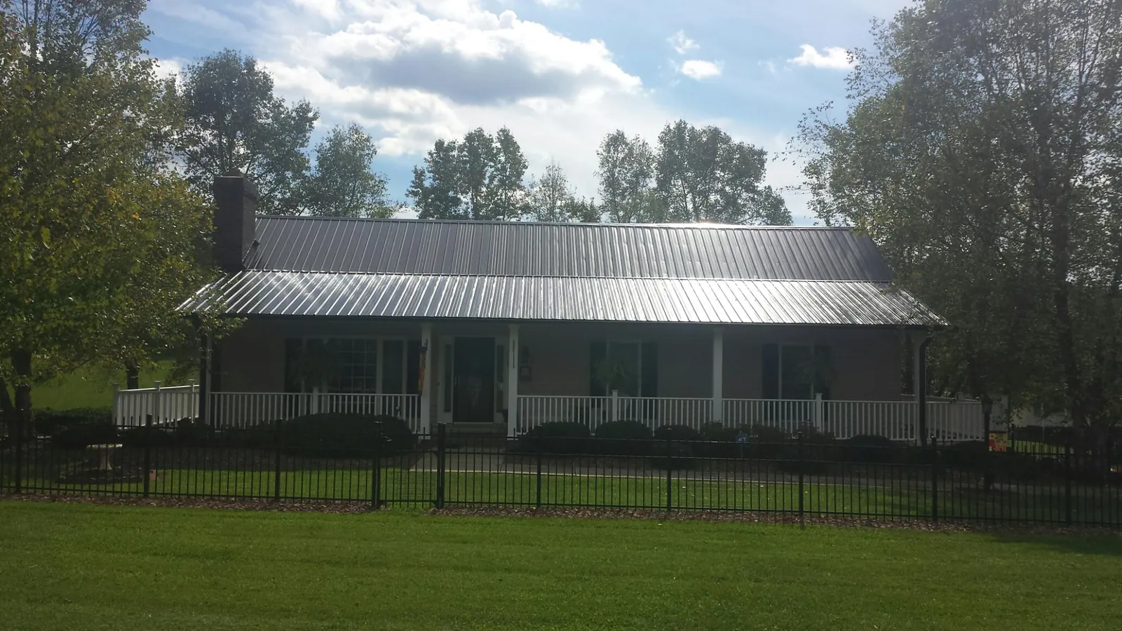 Gray metal roof on a brick ranch with a full width front porch — Gutter Guard Installation work by our crew in South Glens Falls