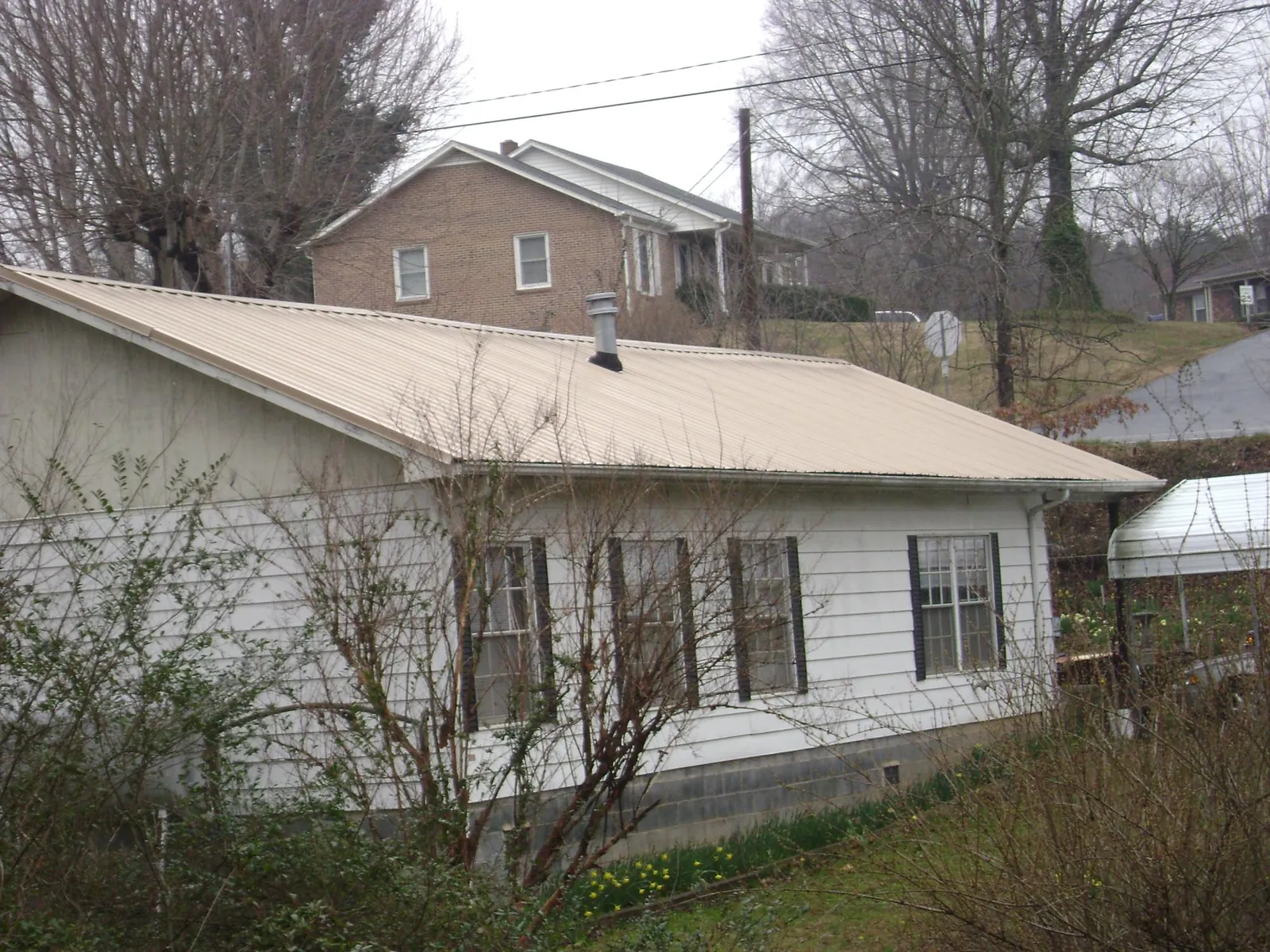 Tan metal roof on a white sided house set into a hillside — Commercial Roofing by Roofing Brothers in South Glens Falls