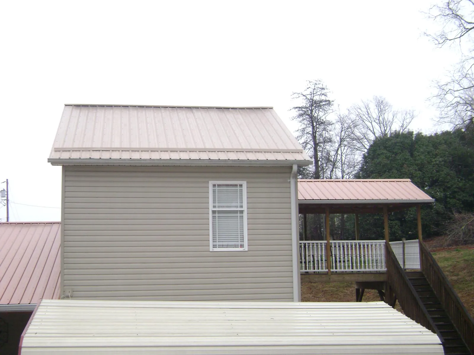 Tan metal roofs on a two story addition and attached porch, from a Roof Replacement job in South Glens Falls