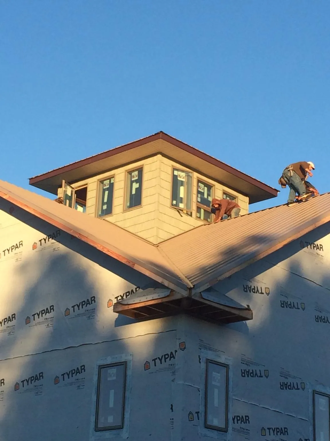 Roofers working around a rooftop cupola on a new metal roof at sunset — Roof Waterproofing in South Glens Falls by Roofing Brothers